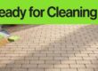 A broom and moved patio items leave brick pavers clear for cleaning.