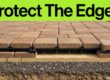 Brick pavers meet a black edge restraint over sand and compacted aggregate.