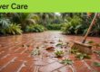 A broom sweeps wet leaves from a terracotta patio beneath a green banner.