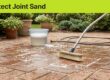 A brush and gentle stream of water clean brick pavers beside a bucket, leaving the sand-filled joints intact.