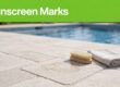 A sunscreen mark on pale pavers beside a brush and folded cloth, with a pool in the background.